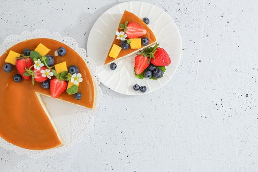 A piece of sliced mango cheesecake on a stand, garnished with berries and flowers. Healthy dessert. Vegetarian food.