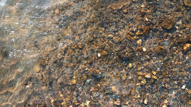 Top view on colorful pebbles covered by water. Close up view of smooth round pebble stones on the beach.