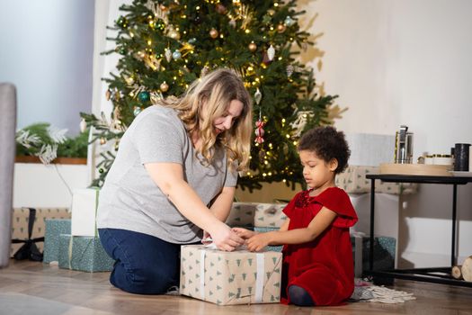 Parent and little child having fun near Christmas tree indoors. Loving family with presents in room.