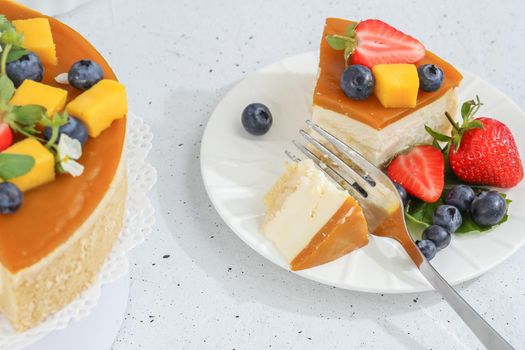 A piece of cheesecake with mango on a plate with a tea fork decorated with berries and flowers on a gray background. Healthy food.