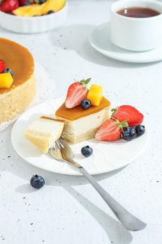 A piece of cheesecake with mango on a plate with a tea fork decorated with berries and flowers on a gray background. Healthy food.