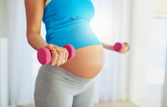 Cropped shot of a pregnant woman working out with weights at home.