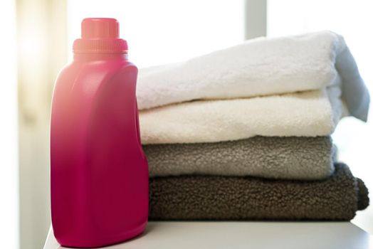 Shot of a bottle of detergent alongside a pile of folded towels at home.