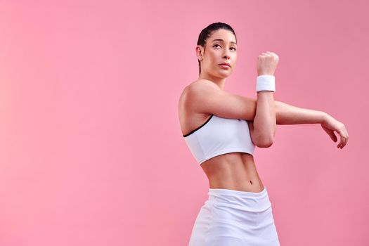 Studio shot of a sporty young woman stretching her arms against a pink background.
