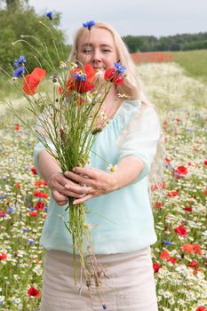 a beautiful middle-aged blonde woman stands among a flowering field of poppy, daisies, Cornflowers, and holds a bouquet of wild flowers and laughs. High quality photo