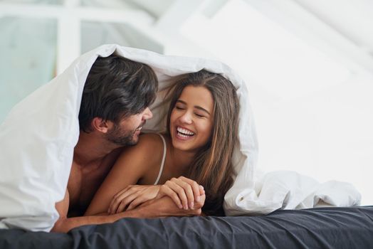 Shot of a happy young couple laying under a duvet together in bed.