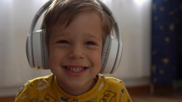 Close up handsome smiling boy listening to music headphones indoor. Children and technology. Love of music, children's dreams hobbies. Talented happy little child leasure. Childhood, musicality, hobby.