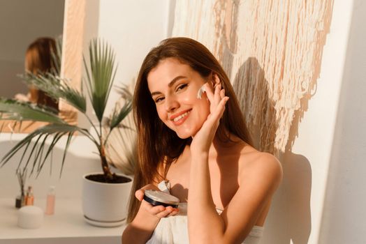 Happy woman doing daily routine moisturizing skin in the morning