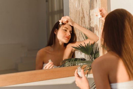 A beautiful young woman uses a moisturizing anti-aging facial serum in the bathroom. Body skin care and cosmetic application concept.