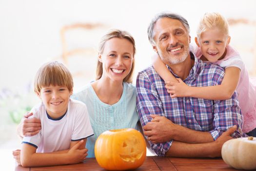 Portrait of a family of four sitting with their jack-o-lantern at home.