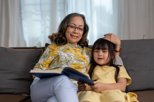 happy asian family grandmother reading to granddaughter book at home.