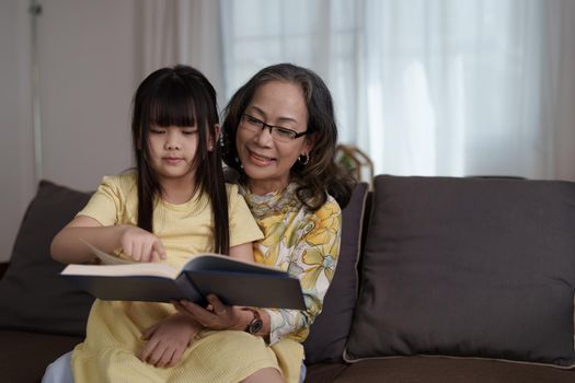 happy asian family grandmother reading to granddaughter book at home.