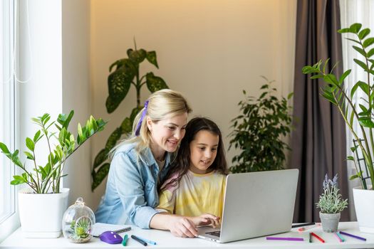 Happy mother with little kid daughter having fun online with application, watching video cartoons or playing game on laptop together, young babysitter or nanny teaching child girl to use computer.