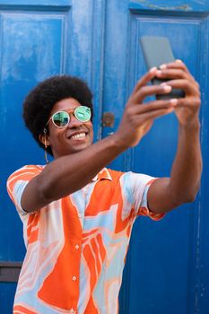 Young happy black man taking selfie with mobile phone outdoors. Vertical image. Lifestyle concept.