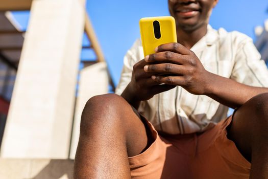 Close up of unrecognizable african american young man sitting on stairs outdoors using mobile phone. Copy space. Lifestyle concept.