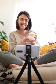 Young caucasian woman DIY influencer showing handmade artisan ceramic vase at camera recording online video. Vertical image. Social media interior design concept.