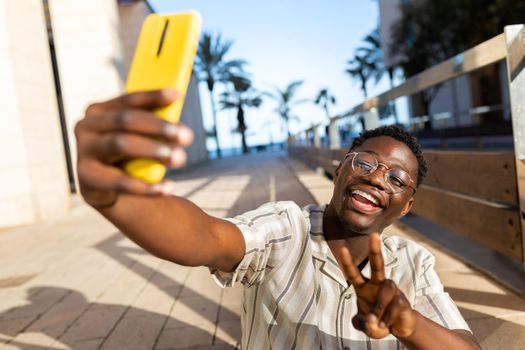 Young black man taking selfie using phone making peace sign. Happy, African american male having fun. Social media concept.