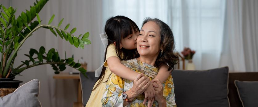 granddaughter kissing with love her mature woman grandmother preschooler at home on sofa.