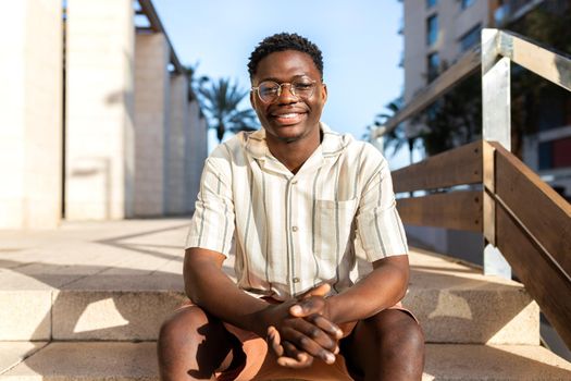 Happy African American young man sitting on stairs outdoors looking at camera. Lifestyle concept.