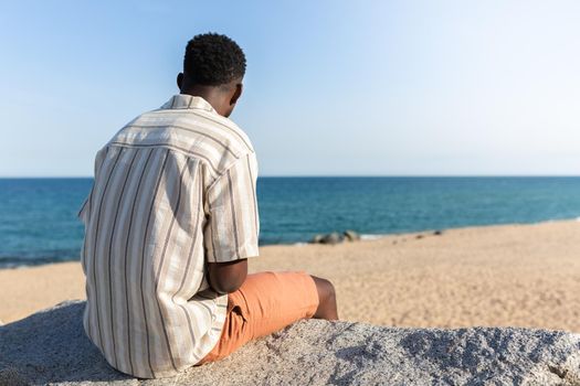 Back view of black man relaxing looking at the ocean. Copy space. Vacation concept.