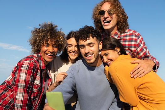 Group of happy young multiracial friends take selfie together using cellphone outdoors. Friendship and technology concept.