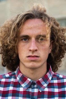Headshot of redhead young caucasian man with curly hair wearing checkered shirt looking at camera. Vertical portrait.