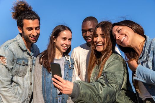 Multiracial friends using mobile phone to look at social media app. Taking selfie. Lifestyle, friendship and social media concept.