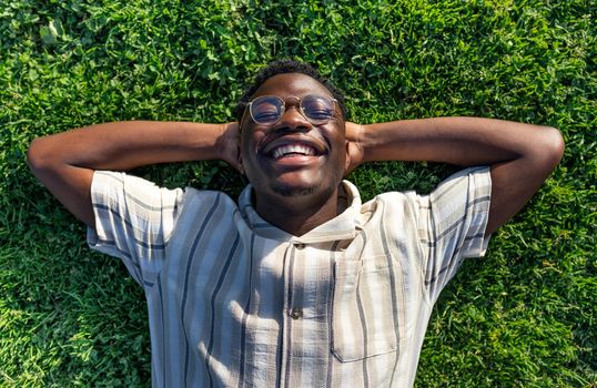 Top view of black man relaxing on grass. Happy black male lying on grass, smiling, enjoying life. Relaxation concept.