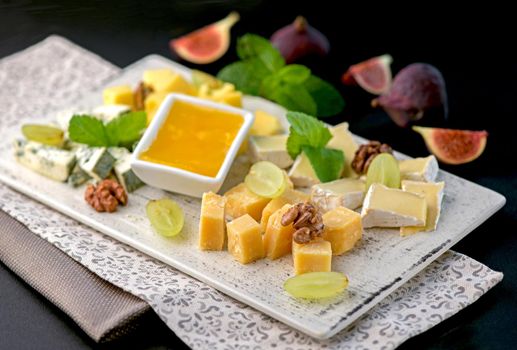 Cheese platter with a variety of types of cheese - gorgonzola, mozzarella, , camembert, toma, emmental and fresh caprino on black background