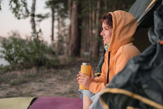 Caucasian woman drinking hot tea from a thermos while resting in a tourist tent