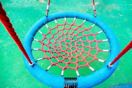 Round swing seat made of mesh in playground. Empty blue and red rope web nest for swinging closeup. High quality photo