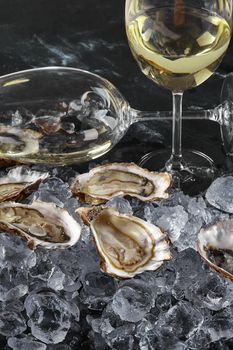 Fresh delicious opened oysters in ice and two glasses of champagne are on a black stone textured background. Delicacies at a restaurant. Healthy sea food. Side view. Close-up shot.