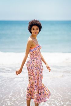 Side view of young female travelling during vacation and enjoying bright summer day while standing on seashore washed by rippling water