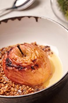 Close-up photo of a gourmet baked apple stuffed with honey and nuts, healthy nutrition, delicious sweet food, gorgeous fruit dessert flavored with cinnamon. Autumn or winter dessert. Served in a deep bowl. Cooking concept.