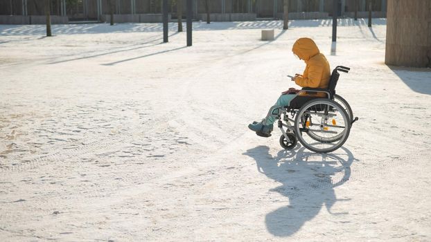 Caucasian woman in a wheelchair uses a smartphone on a walk in the park in winter