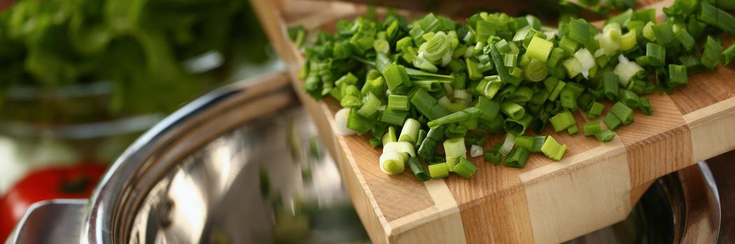 Put chopped green onions in a saucepan, close-up. Cooking at home, delicious fresh food ingredient, organic product