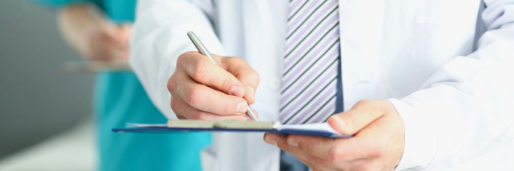 The doctor holds a folder in his hands and writes, close-up, blurred background. Medical professionals make records of diseases, write prescriptions