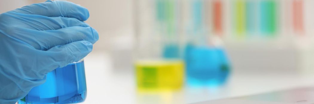 Microbiologist hands in gloves hold blue liquid, close-up, blurry background. Chemical experiments in the laboratory