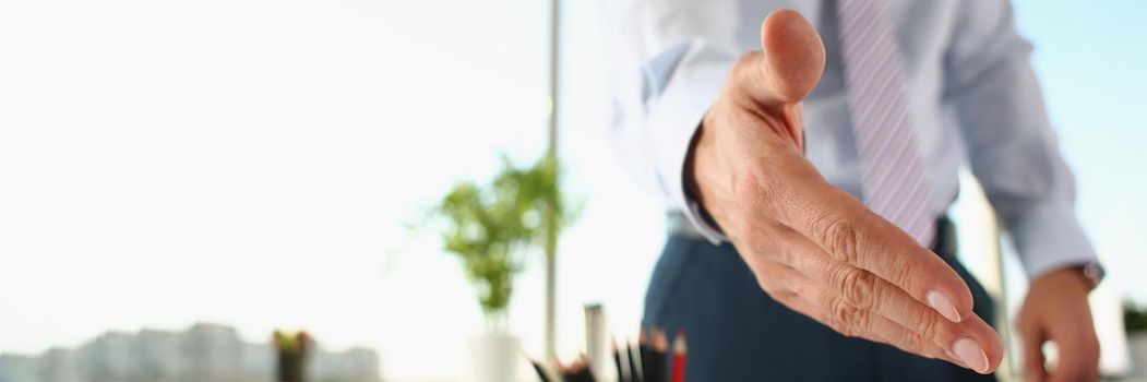 A man stretches out his hand for a handshake, close-up, blurry. Hiring, friendly office atmosphere, employee greetings