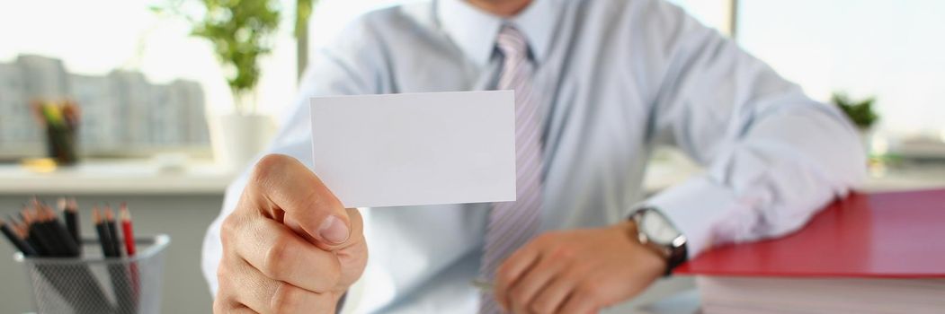 A man in the office holds out a business card, close-up, blurry. Printing services, business cooperation, business acquaintance