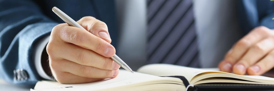 A man in a suit writes in a notebook, close-up. Planning daily activities, businessman's diary. Planner book