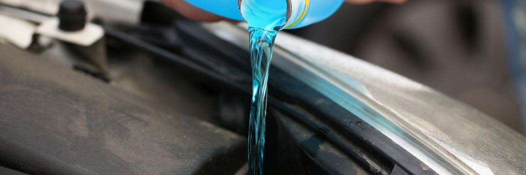 A man pours antifreeze from a canister into a car engine, close-up. Blue coolant, anti-corrosion properties, service station