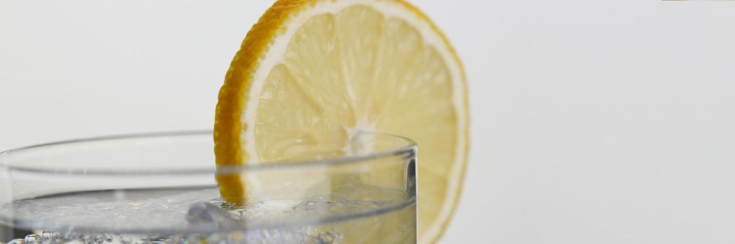 A glass of soda water with a slice of lemon, close-up. Toning drink with ice on gray background, slimming product