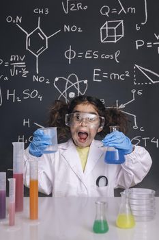 funny scientist girl with gloves and goggles in lab coat with chemical flasks, blackboard background with science formulas, explosion in the laboratory, back to school concept, vertical photo