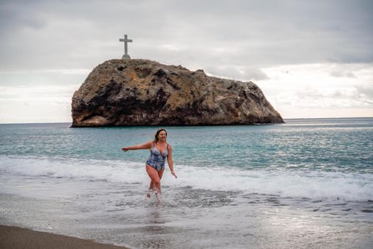 A plump woman in a bathing suit enters the water during the surf. Alone on the beach, Gray sky in the clouds, swimming in winter