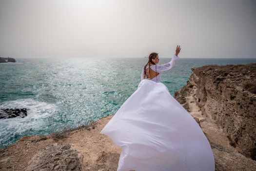 Happy freedom woman on the beach enjoying and posing in white dress. Rear view of a girl in a fluttering white dress in the wind. Holidays, holidays at sea