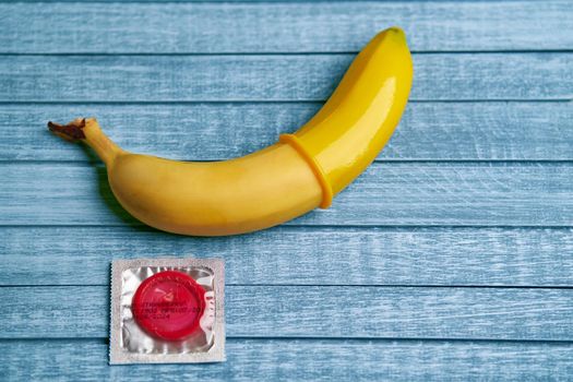 Red Condom and yellow banana lays on a blue wooden background