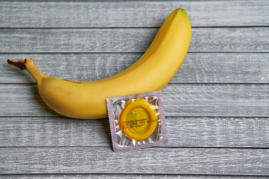 Yellow Condom and yellow banana lays on a gray wooden background