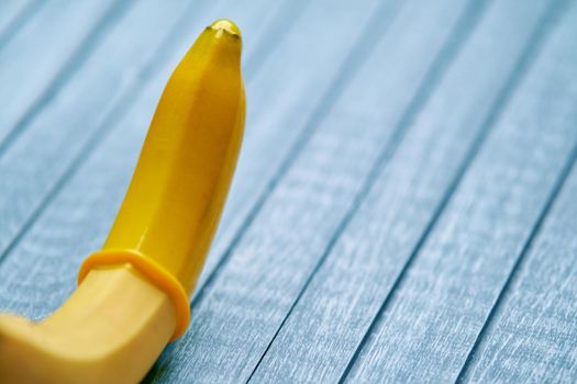 Yellow Condom and yellow banana lays on a blue wooden background