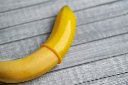 Yellow Condom and yellow banana lays on a gray wooden background